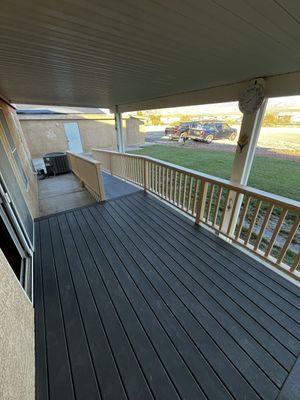 Covered wooden deck with railing and ramp leading to a grassy yard, viewed from under the roof