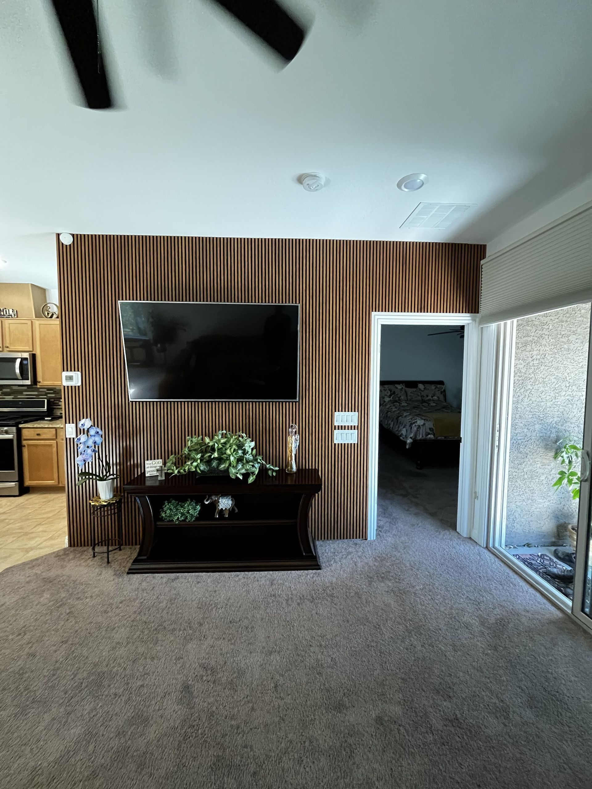 Living room with wall-mounted TV, striped wood accent wall, dark console, and sliding glass door