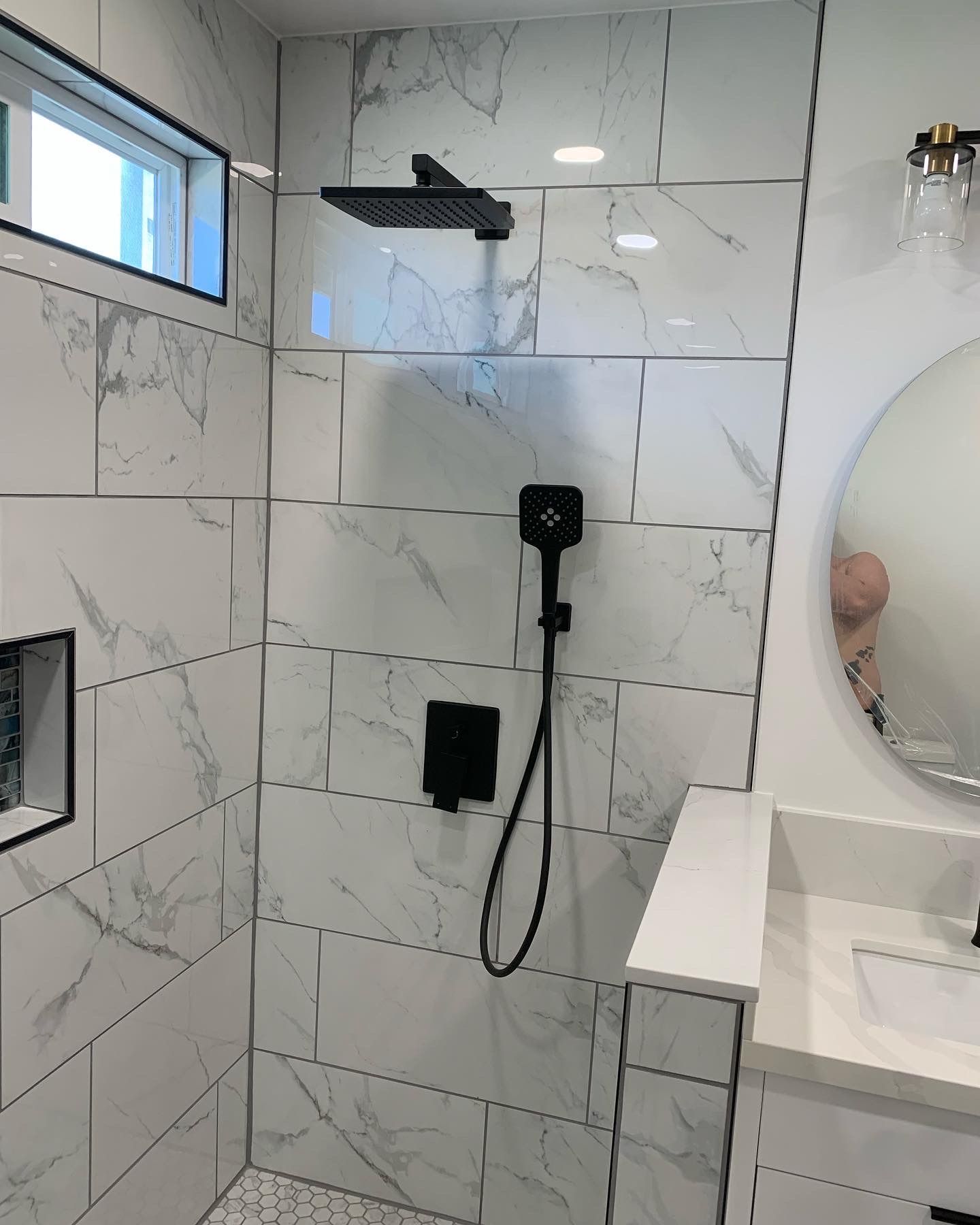 Modern white marble-tiled bathroom shower with black fixtures and a wall mirror