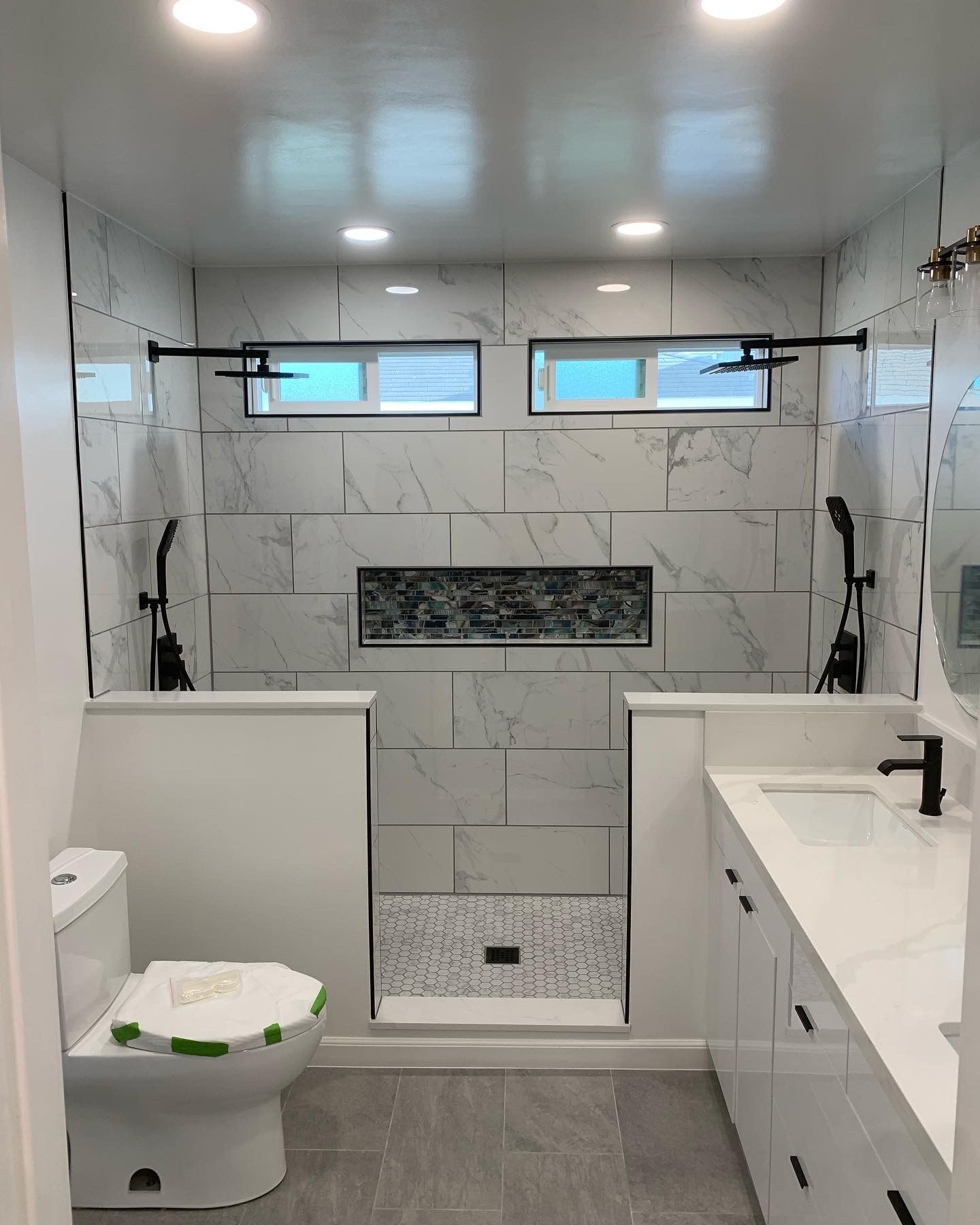 Modern white-tiled bathroom with toilet, vanity, and walk-in shower with bench and windows