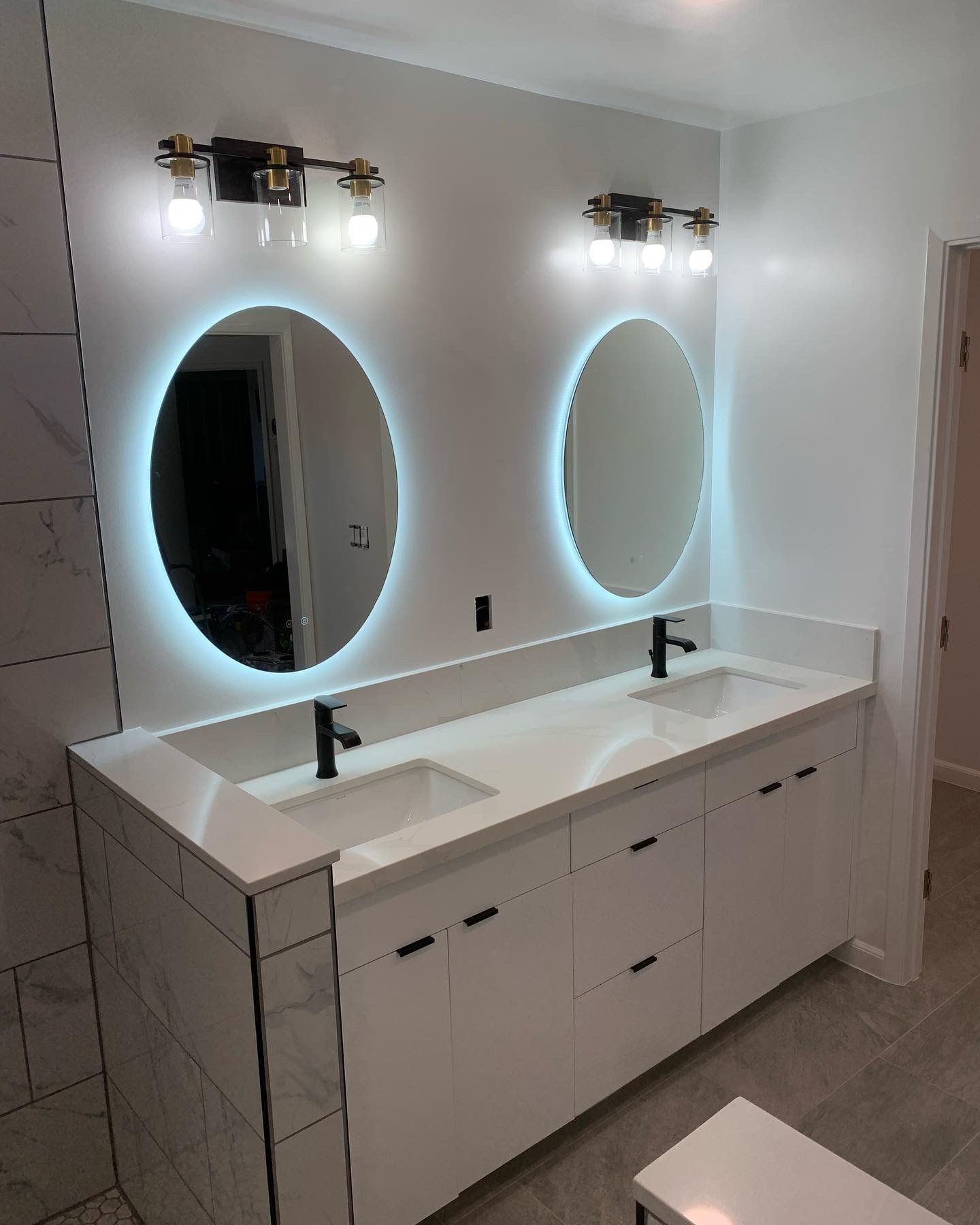 Modern double-sink bathroom vanity with oval LED mirrors, white cabinetry, and chrome fixtures.