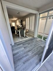 Open sliding glass doors to a bright room with gray flooring and a dining area beyond.