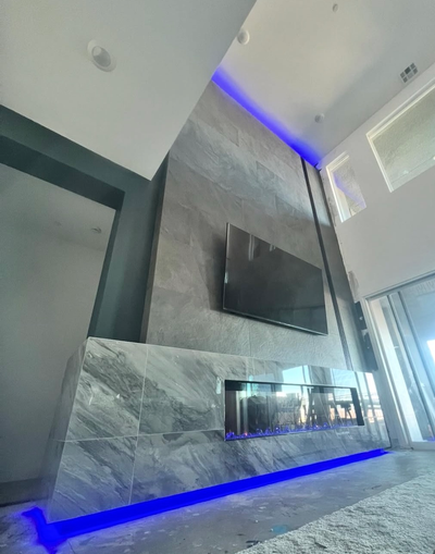 Modern living room with a gray stone accent wall, wall-mounted TV, fireplace, and blue LED lighting