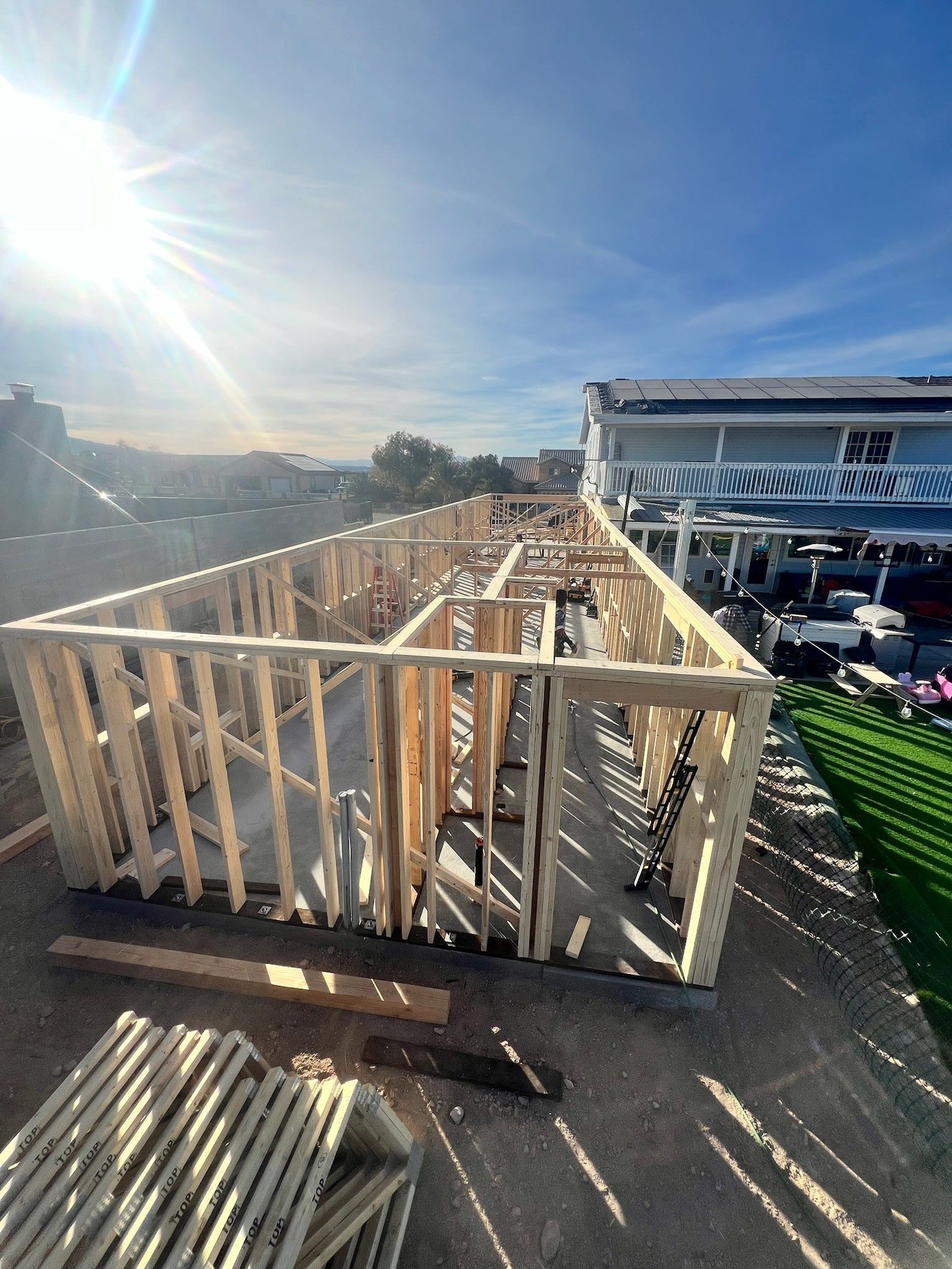 Wood-framed platform under construction on a rooftop, with bright sun and a building in the background.