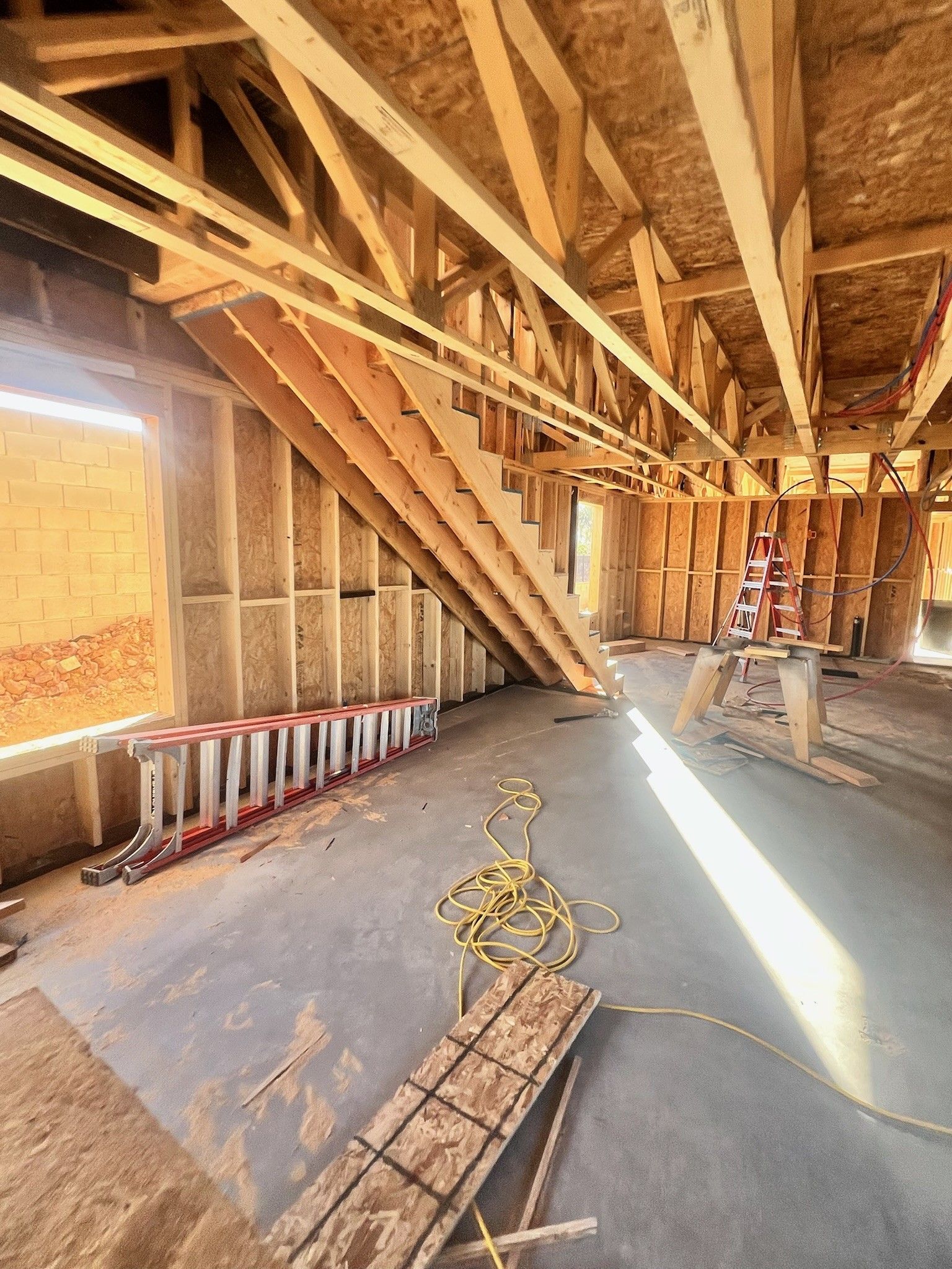 Unfinished attic with exposed wooden rafters, stairs, insulation, and sunlight on the floor