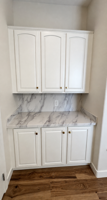 White built-in kitchen cabinets and marble-pattern backsplash with wood flooring.