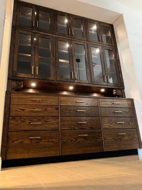 Dark wooden cabinet with glass upper doors and many drawers in a room with a light wood floor