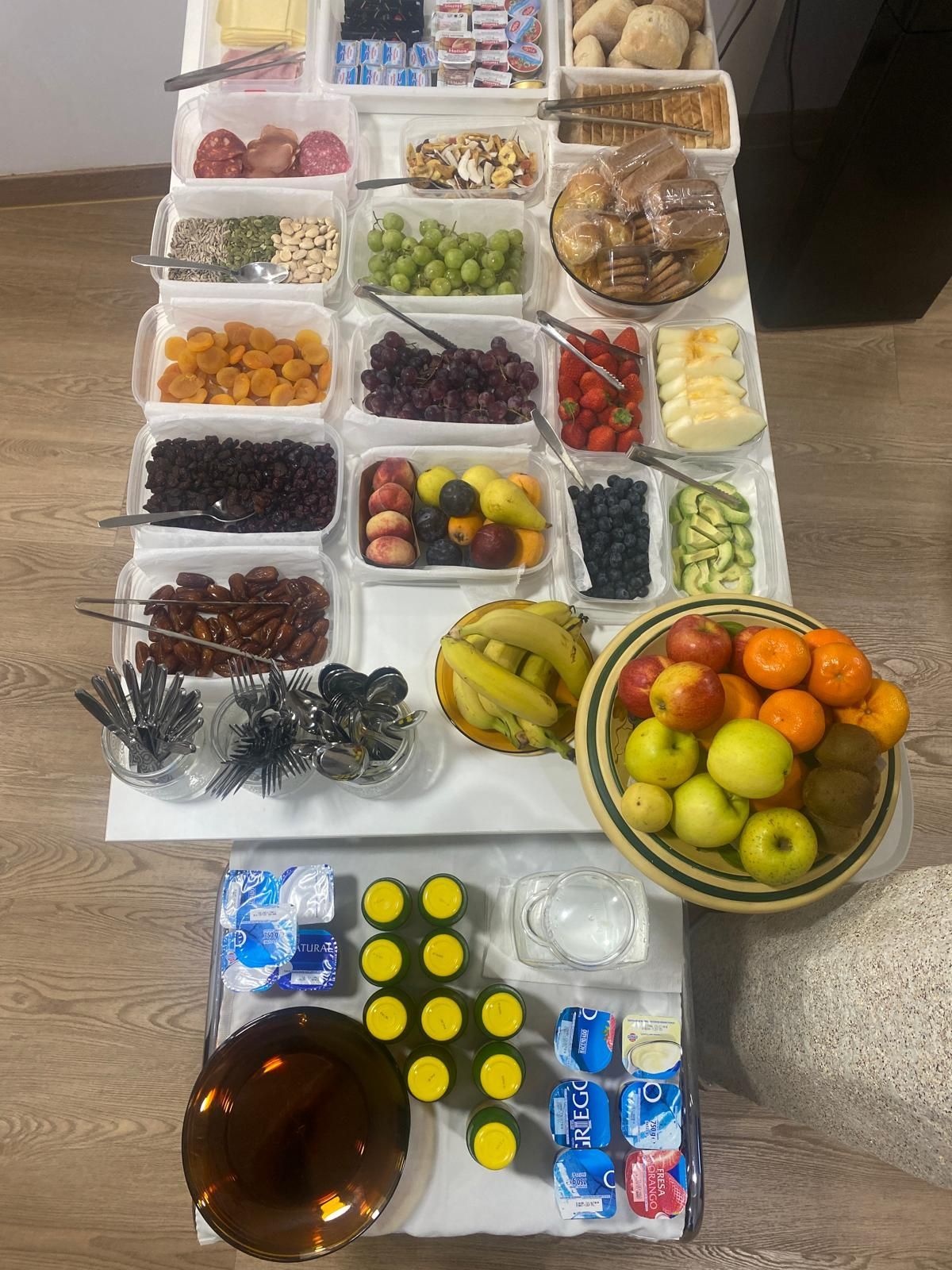 Variedad de frutas y dulces dispuestos sobre una mesa, con un cuenco de naranjas y manzanas delante.