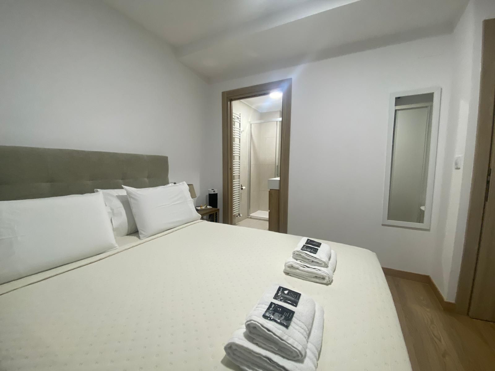 Habitación pequeña de color blanco con una cama, toallas dobladas y un espejo en la pared.