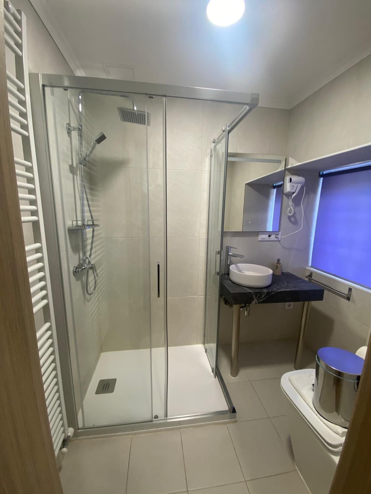 Baño moderno con ducha a ras de suelo, lavabo con tocador, inodoro y espejo grande bajo una iluminación brillante.