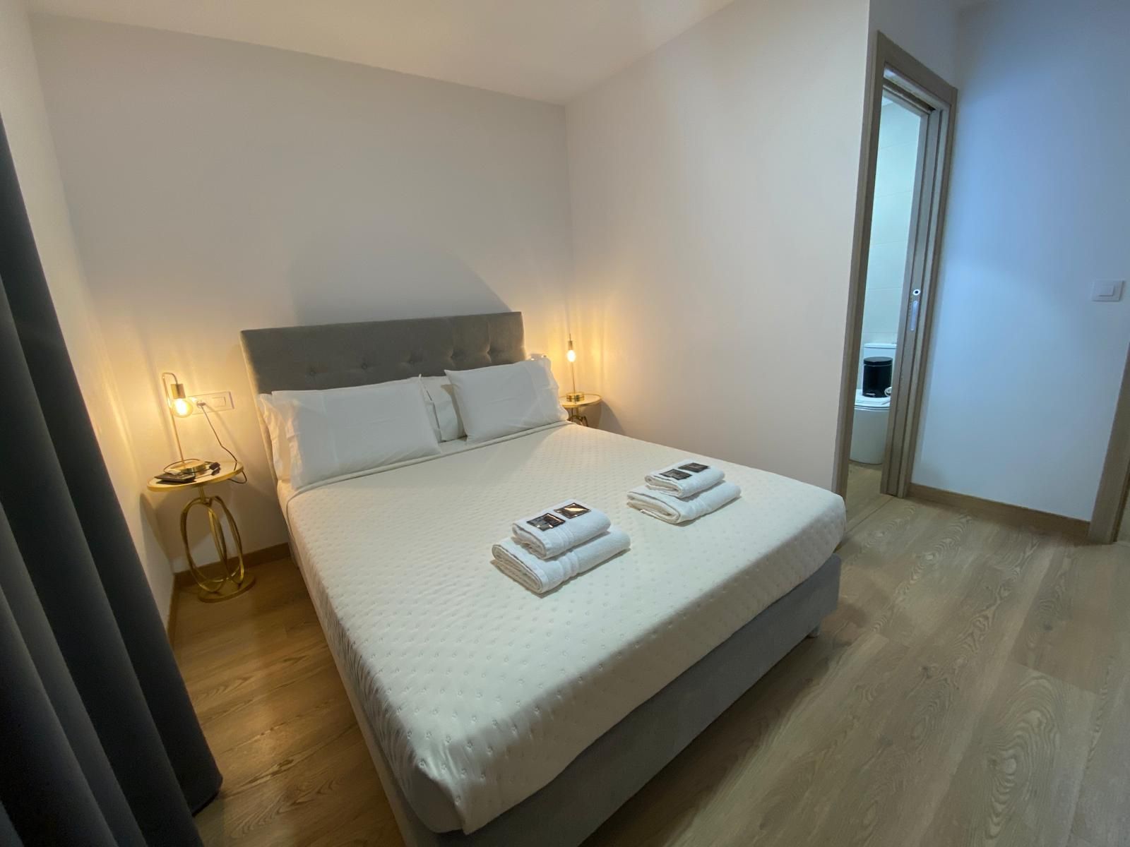 Dormitorio minimalista con una cama, lámparas de noche y toallas dobladas encima.