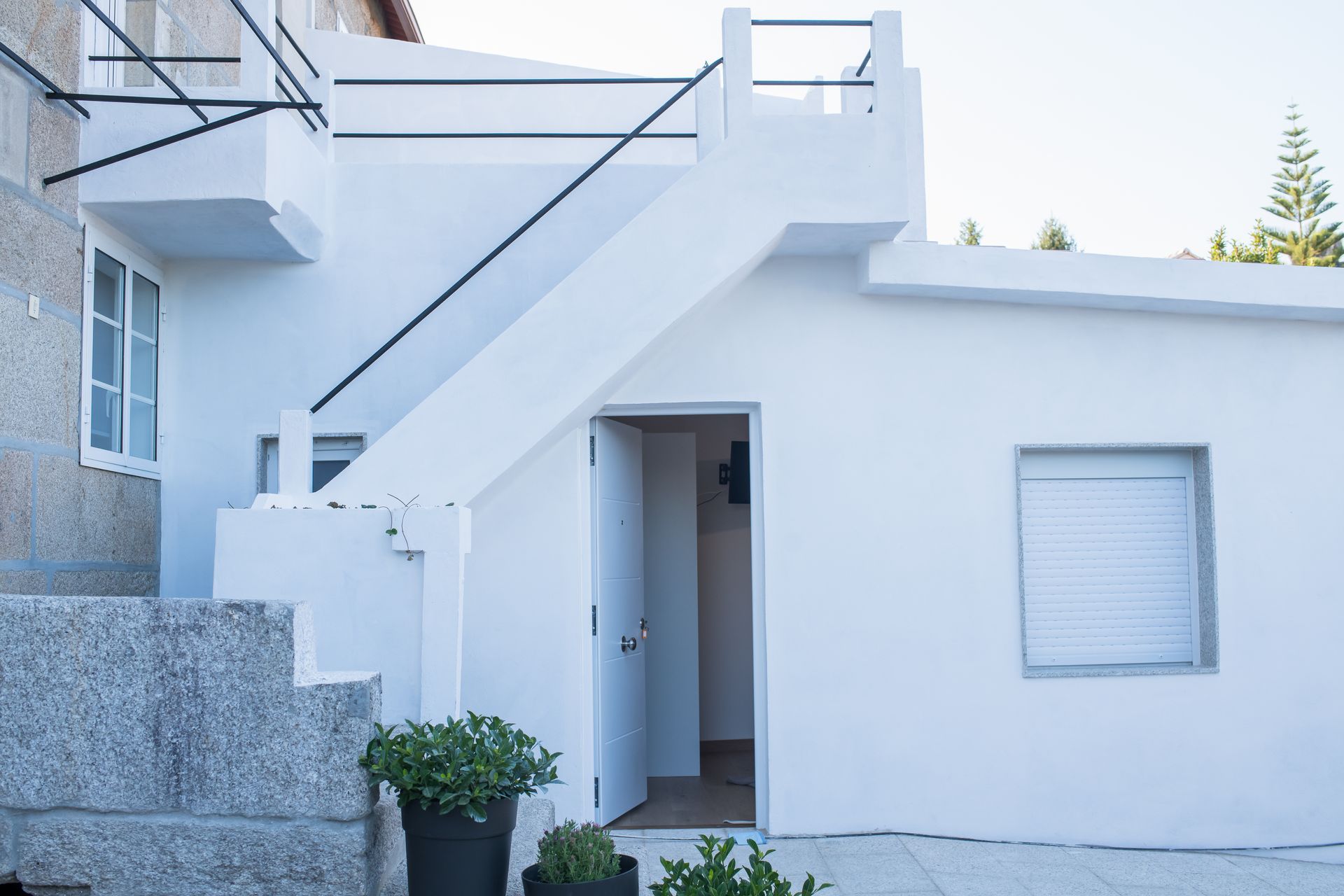 Entrada de casa de estuco blanco con escaleras, balcón y una pequeña ventana.