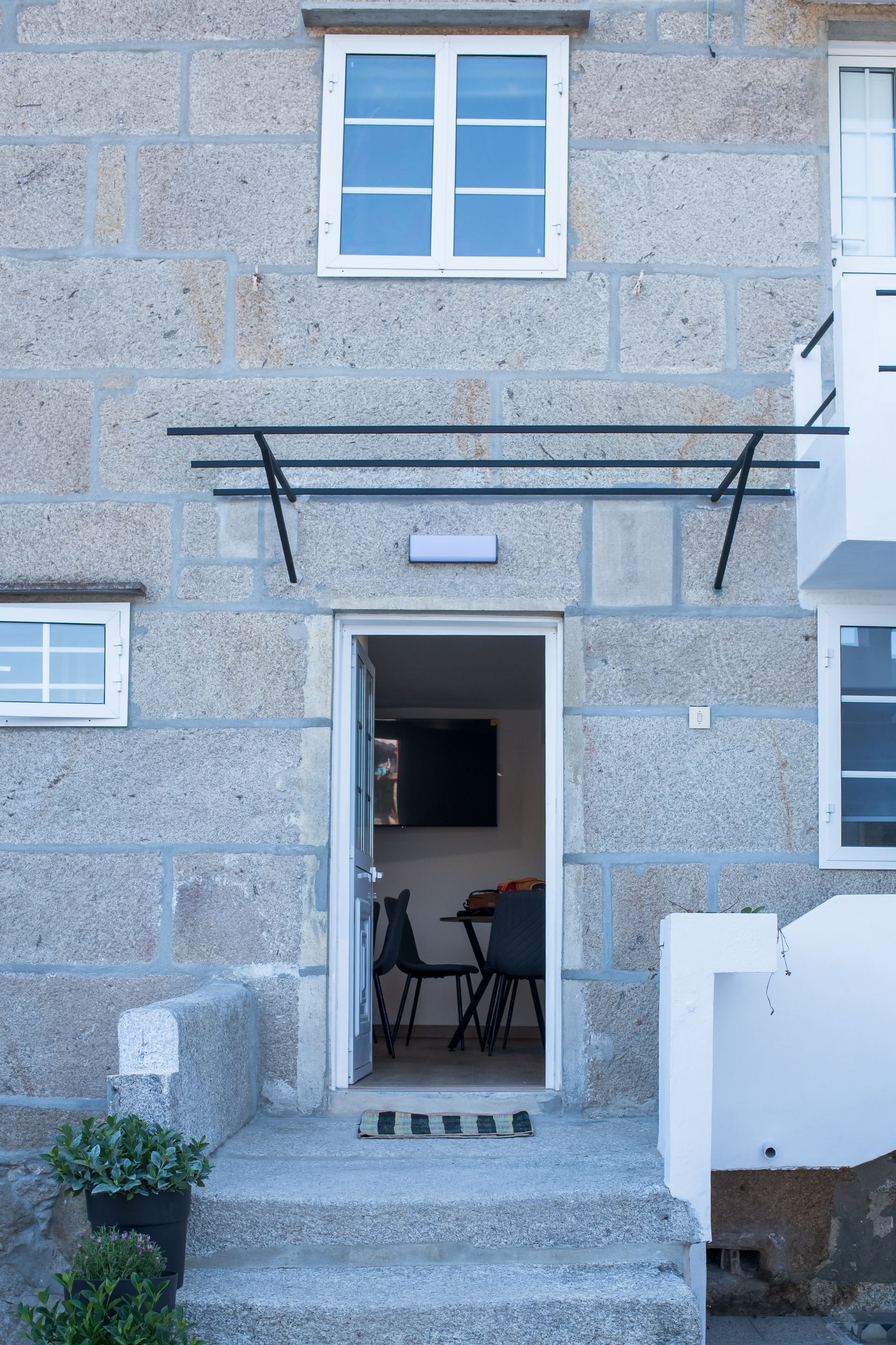 Entrada de piedra a la casa con escalones, puerta abierta y toldo de metal sobre la entrada.