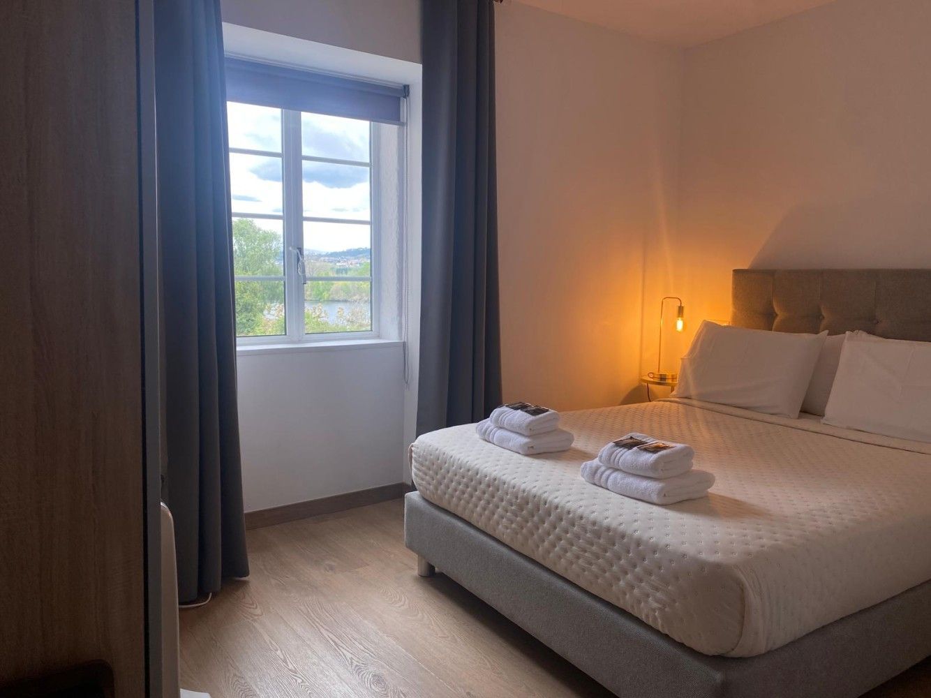 Habitación acogedora con cama grande, luz cálida de lámpara y ventana con vistas al exterior.