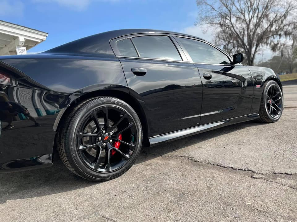 Black sports sedan with tinted windows and black wheels parked on a sunny street.