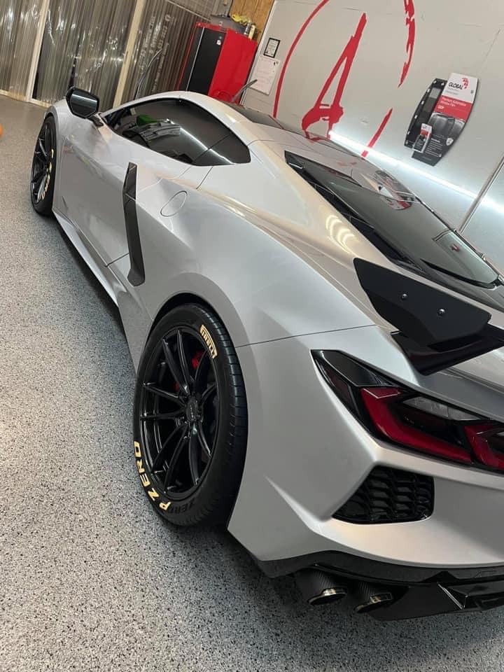 Silver sports car parked in a garage, shown from the rear side with black rims and red taillights