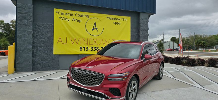 Red SUV parked in front of a yellow AWM window sign on a gray building.