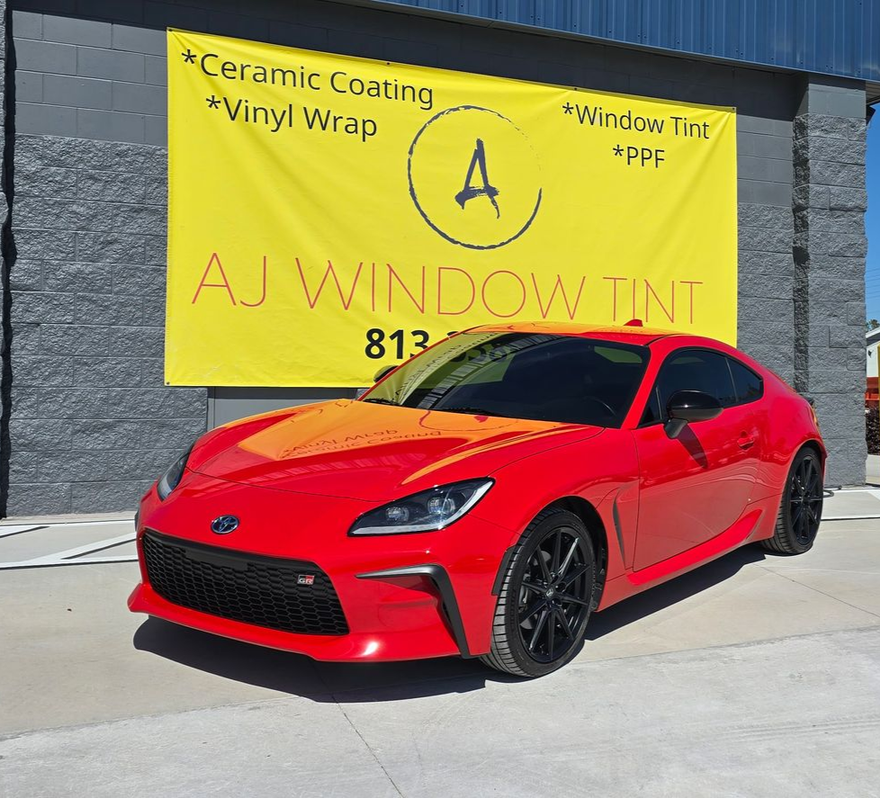 Red sports car parked in front of an AJ Window Tint storefront sign