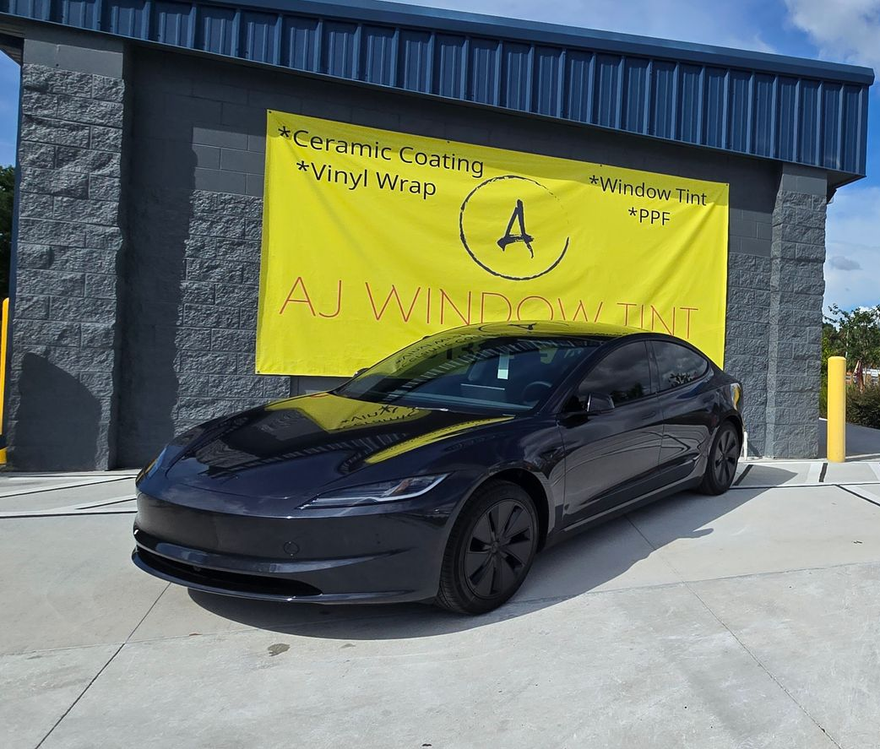 Black sports car parked outside a building with a bright yellow banner behind it.