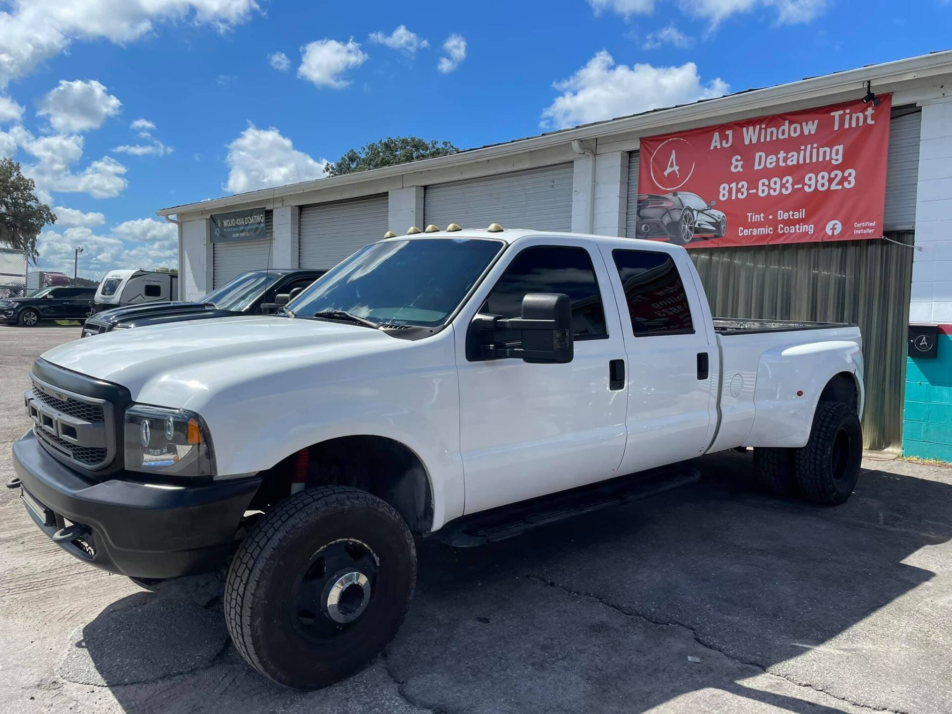 White heavy-duty pickup truck parked outside a repair shop under a red sign.