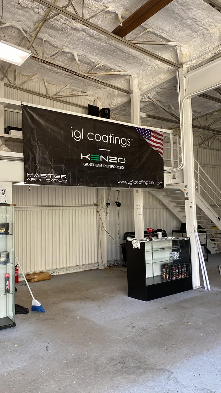 Indoor garage booth with “ig coatings” banner, equipment, and a black counter under exposed beams
