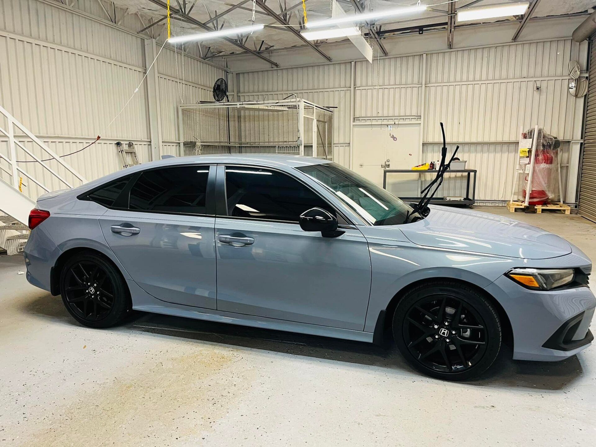 Gray sedan with black rims parked inside a bright garage or auto shop