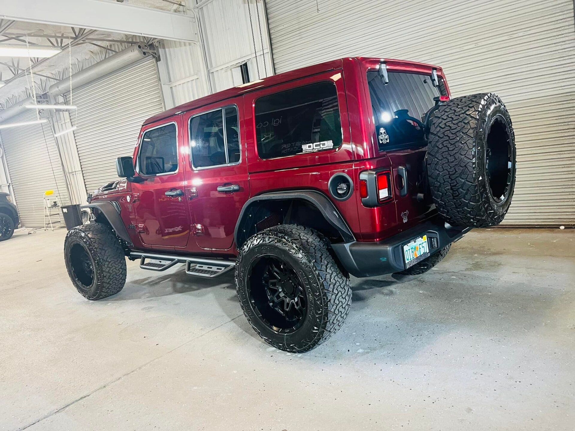 Red Jeep Wrangler on off-road tires, parked indoors in a garage-like space.