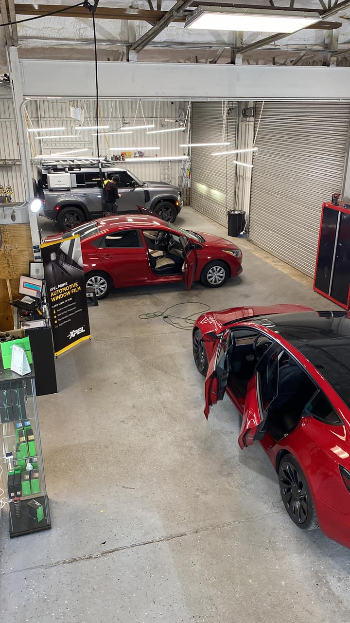Auto shop with several red cars parked indoors, one with its door open under bright lights.
