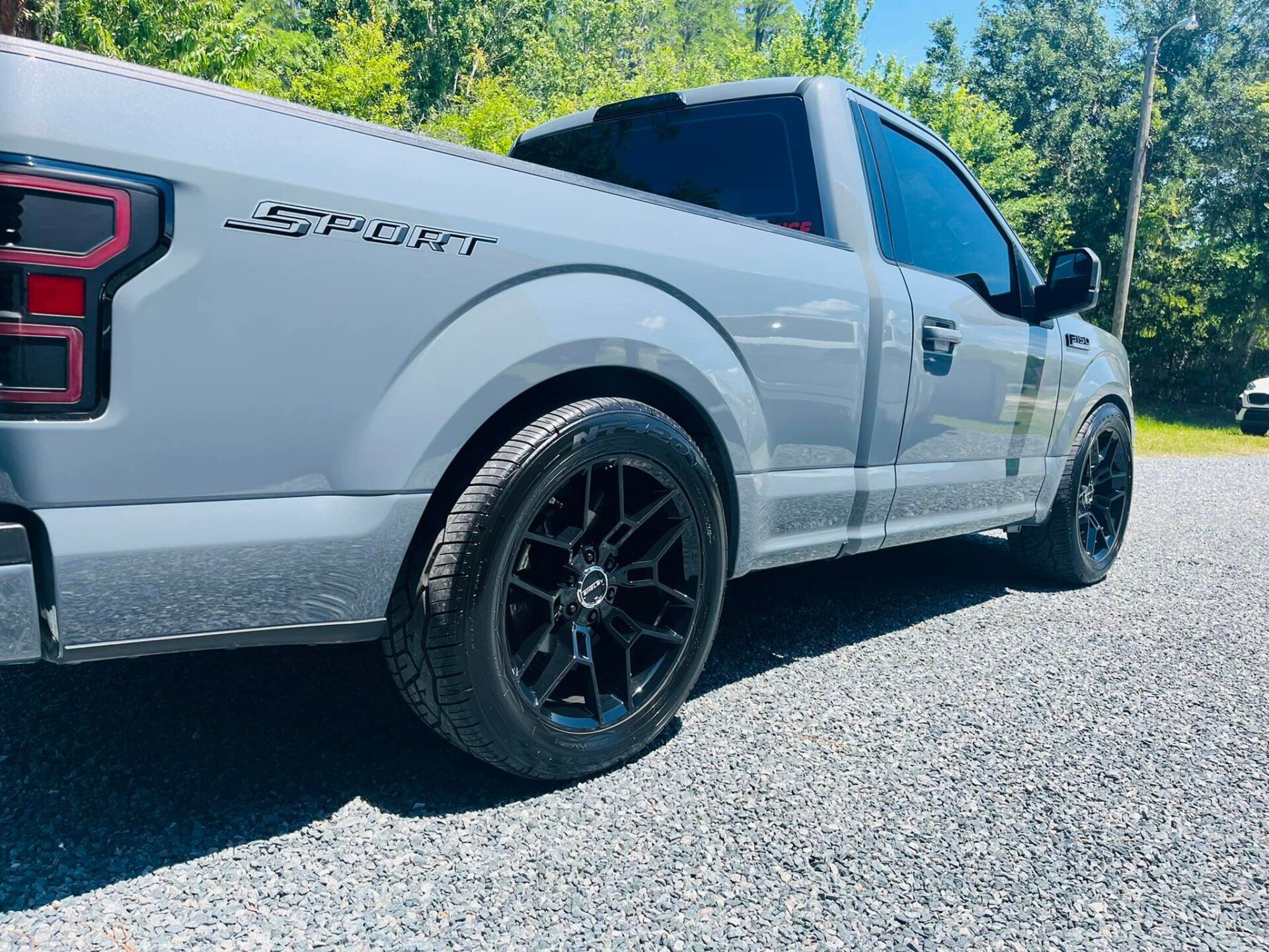 White pickup truck with black rims parked on gravel near trees under a sunny sky