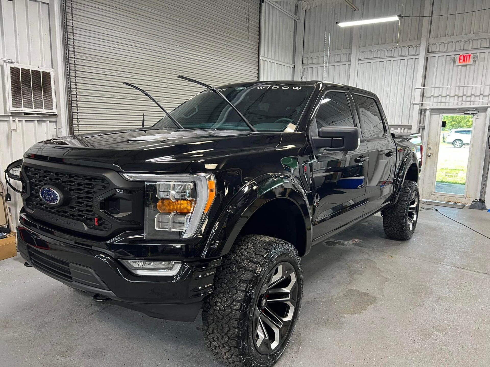 Black lifted Ford pickup truck in a garage, front view with chrome wheels and hood open.