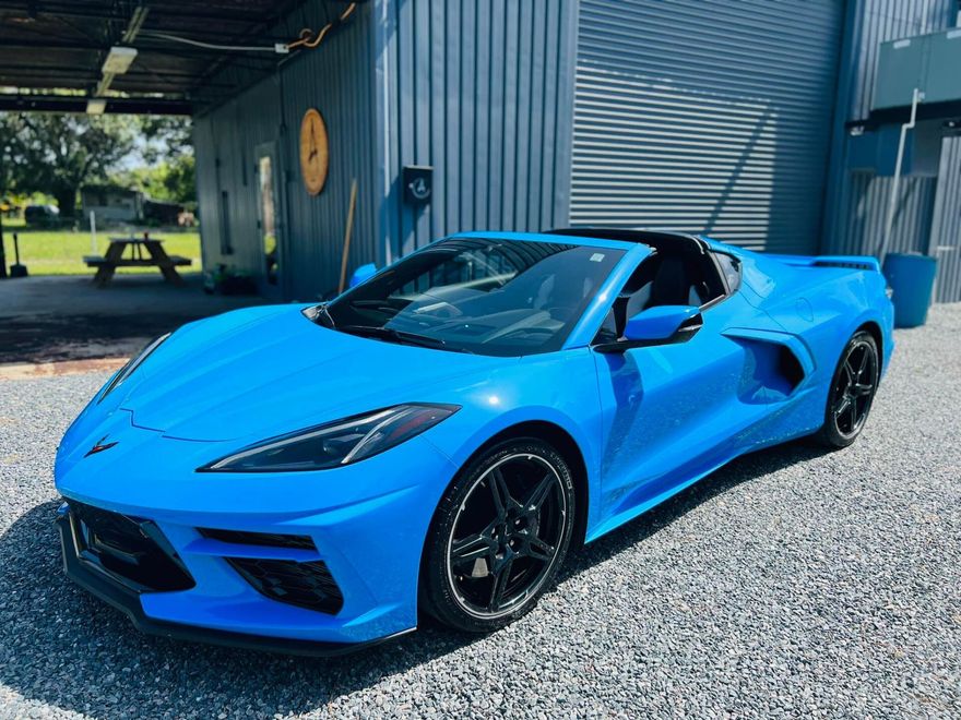 Bright blue sports car parked outside a building on a gravel lot