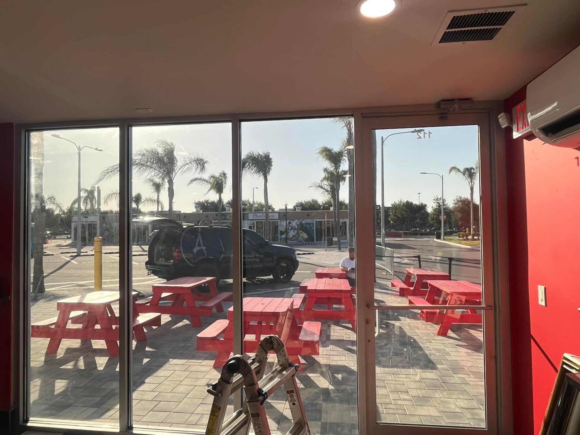 Interior view of a red cafe with red picnic tables outside and glass doors opening to a sunny sidewalk