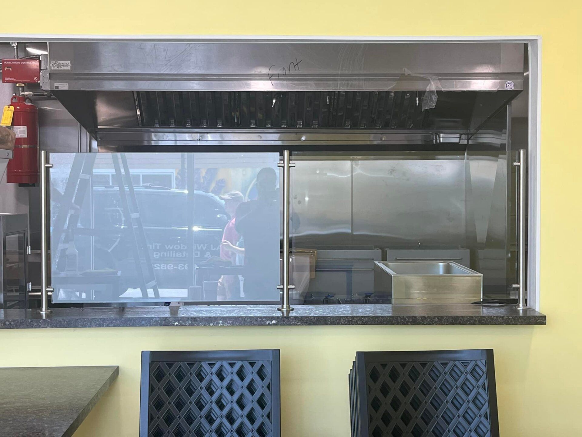 Commercial kitchen pass-through window with stainless steel counter and blue chairs in front