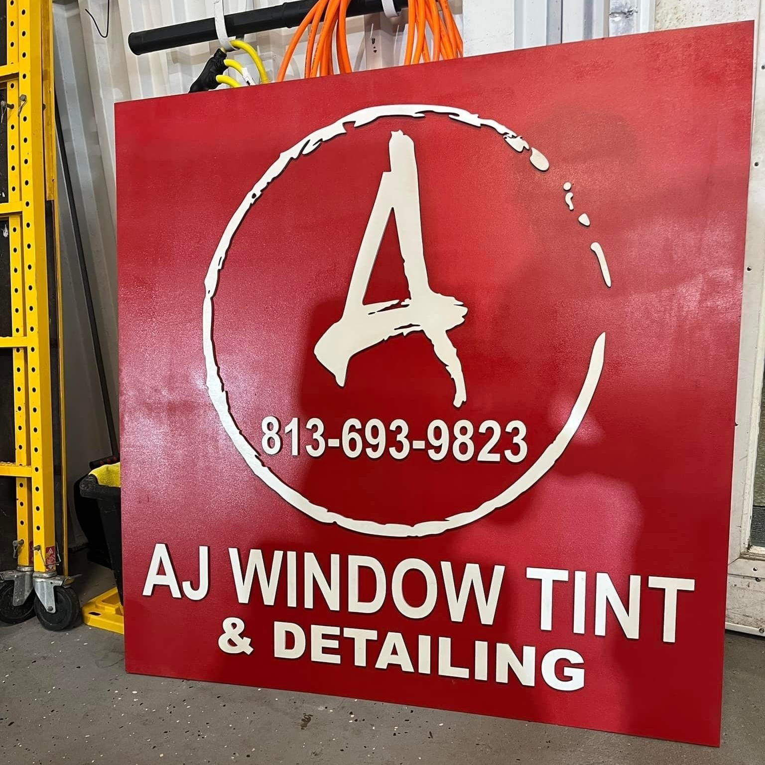 Red sign for AJ Window Tint & Detailing with white logo and phone number 813-693-9823