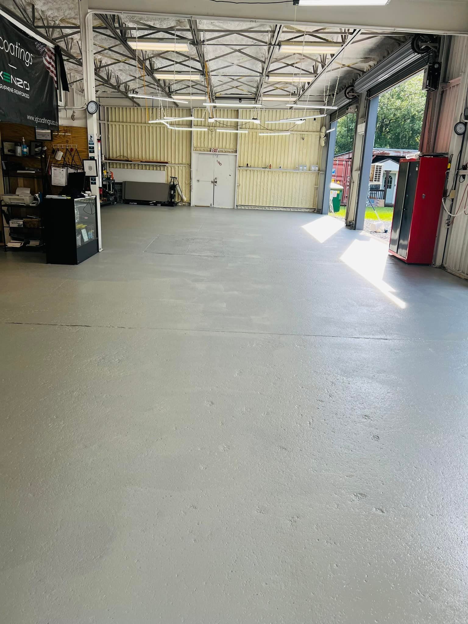 Empty garage bay with concrete floor, open side doorway, and storage shelves along the back wall