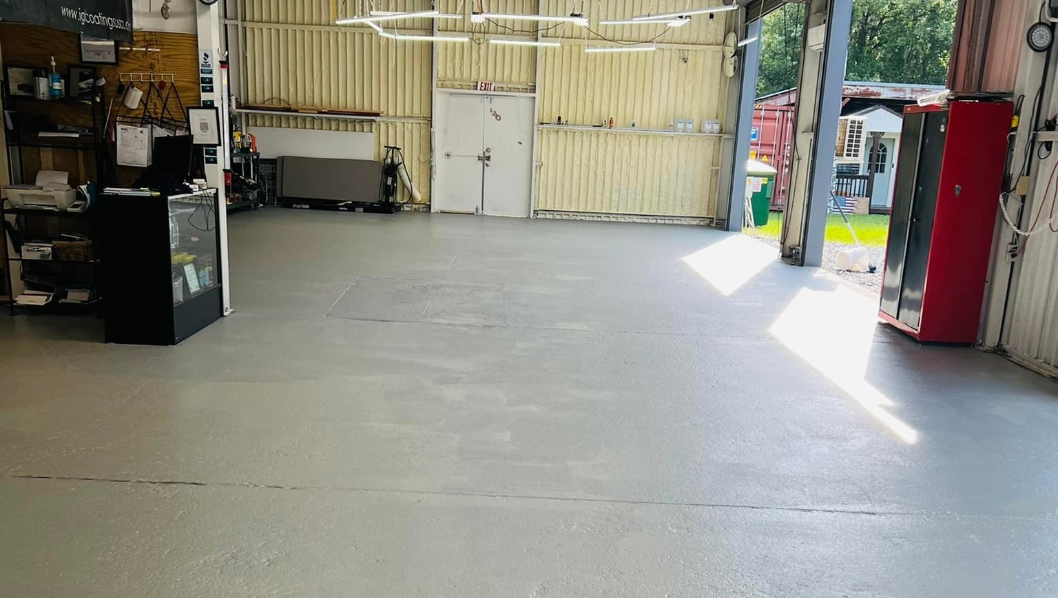 Empty indoor garage with a concrete floor, a black cabinet on the left, and an open doorway to the right.