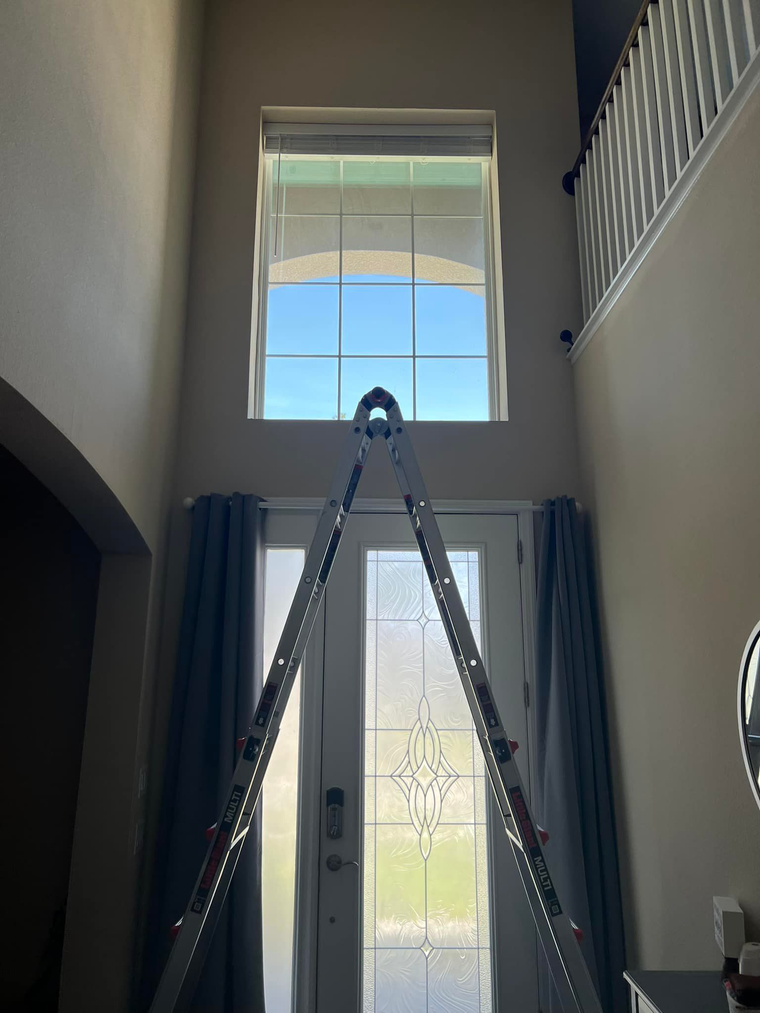 Stairwell with a ladder reaching a second-floor window above a front door.