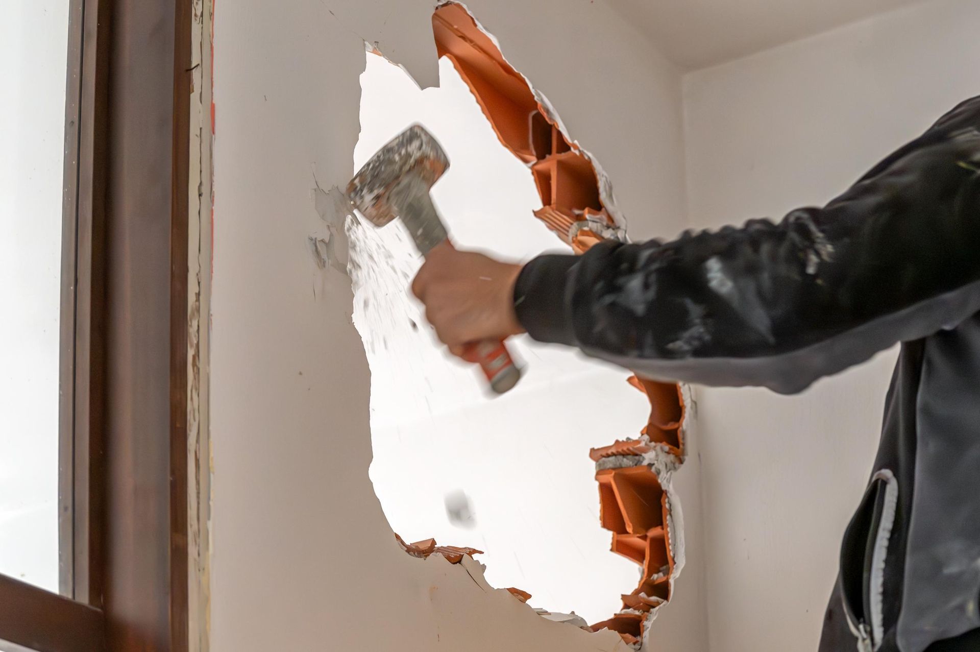 Person using a trowel to patch a large hole in a white interior wall with orange insulation exposed