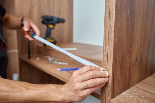 Person measuring a wooden cabinet shelf with a tape measure during assembly