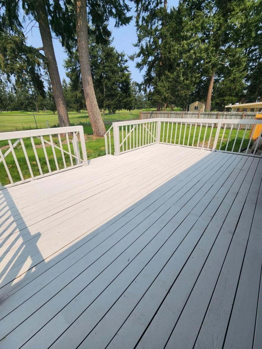 White wooden deck with railing overlooking a grassy yard and trees in sunlight