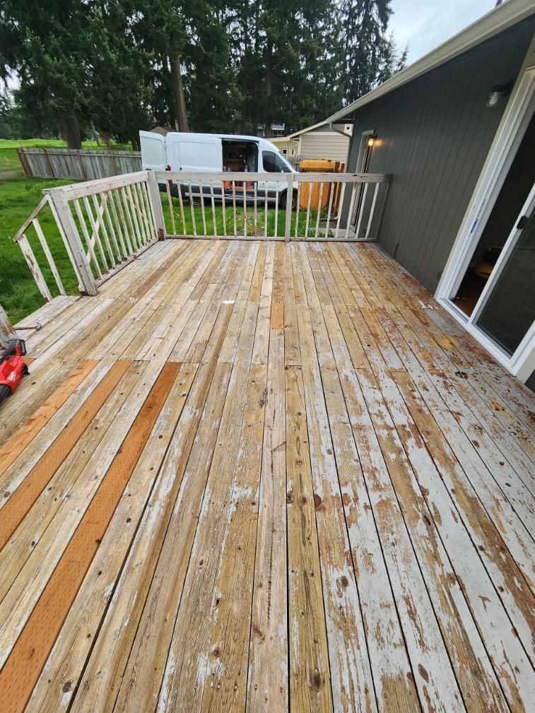 Weathered wooden deck with white railing beside a house, and a white van parked beyond the yard.