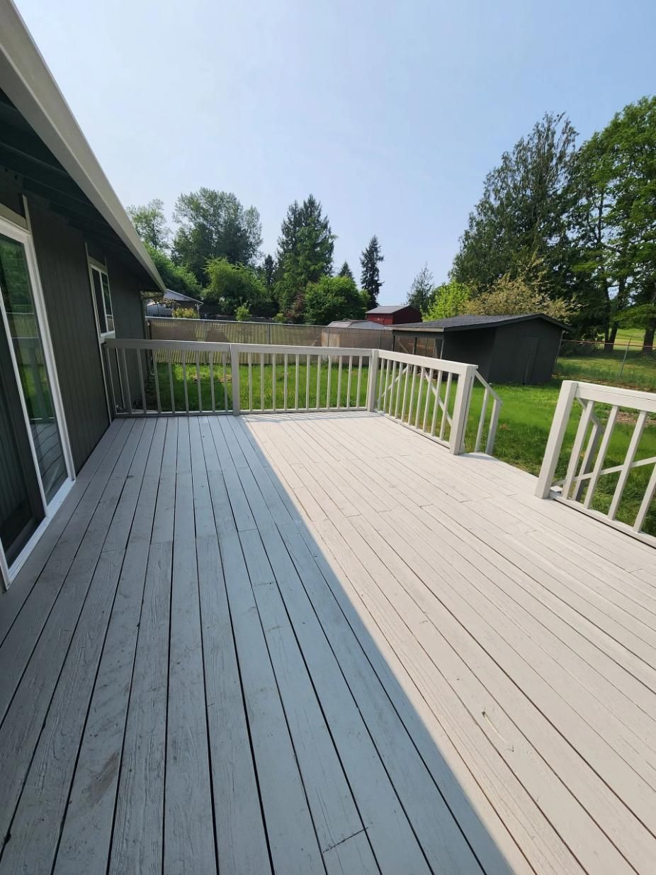 Outdoor wooden deck with white railings, gray and beige planks, and a green backyard view