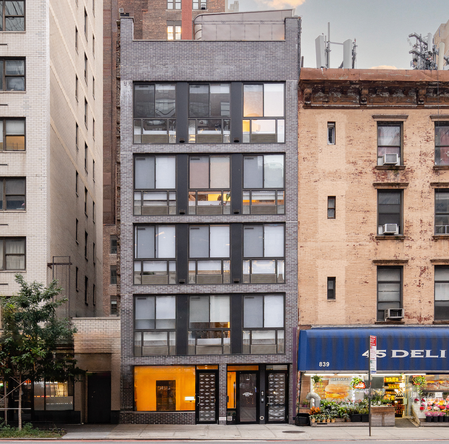 A narrow, multi-story building in New York City with dark windows and brick facade above a deli.