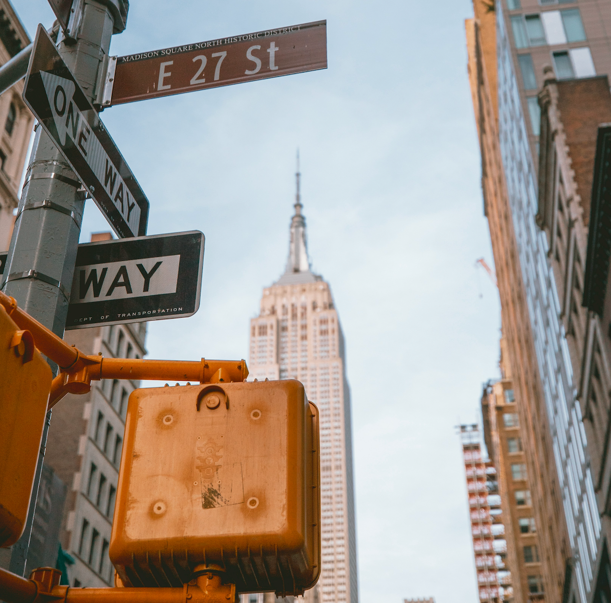 A street sign pointing toward E 27 St in New York City with the Empire State Building in the background.