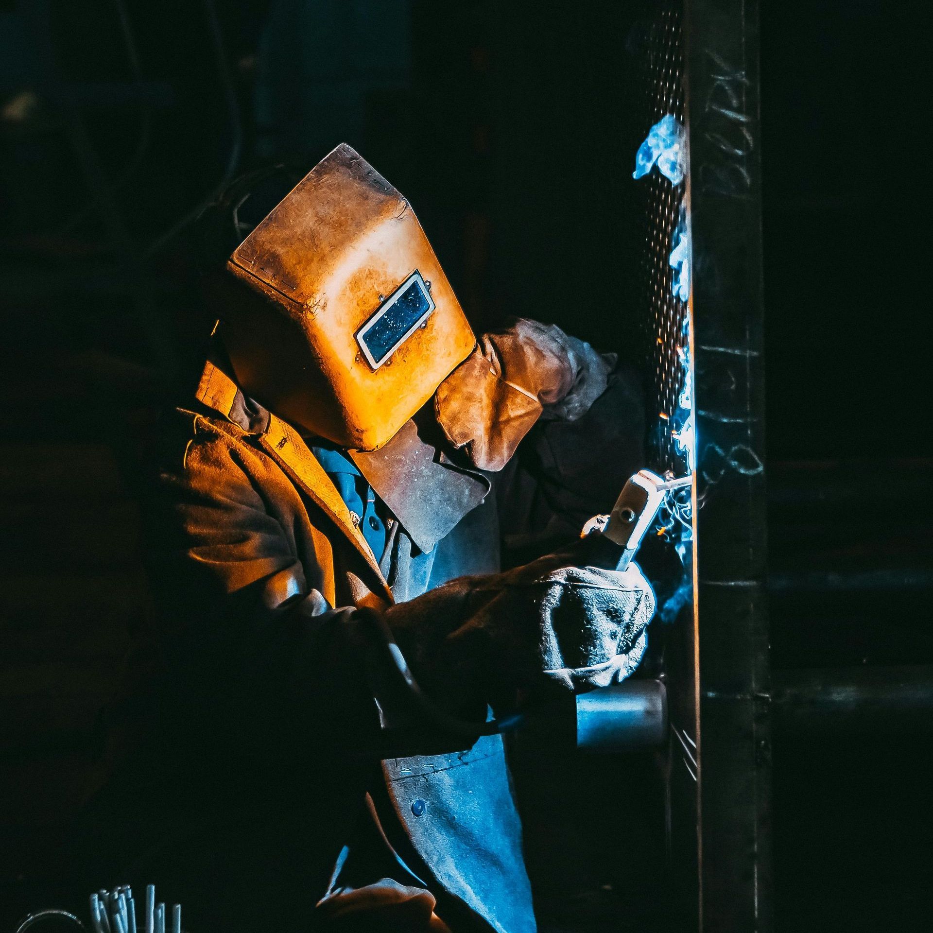 a Welder welding metal in a dimly lit workshop. BSIS for all Welding Inspectors Services