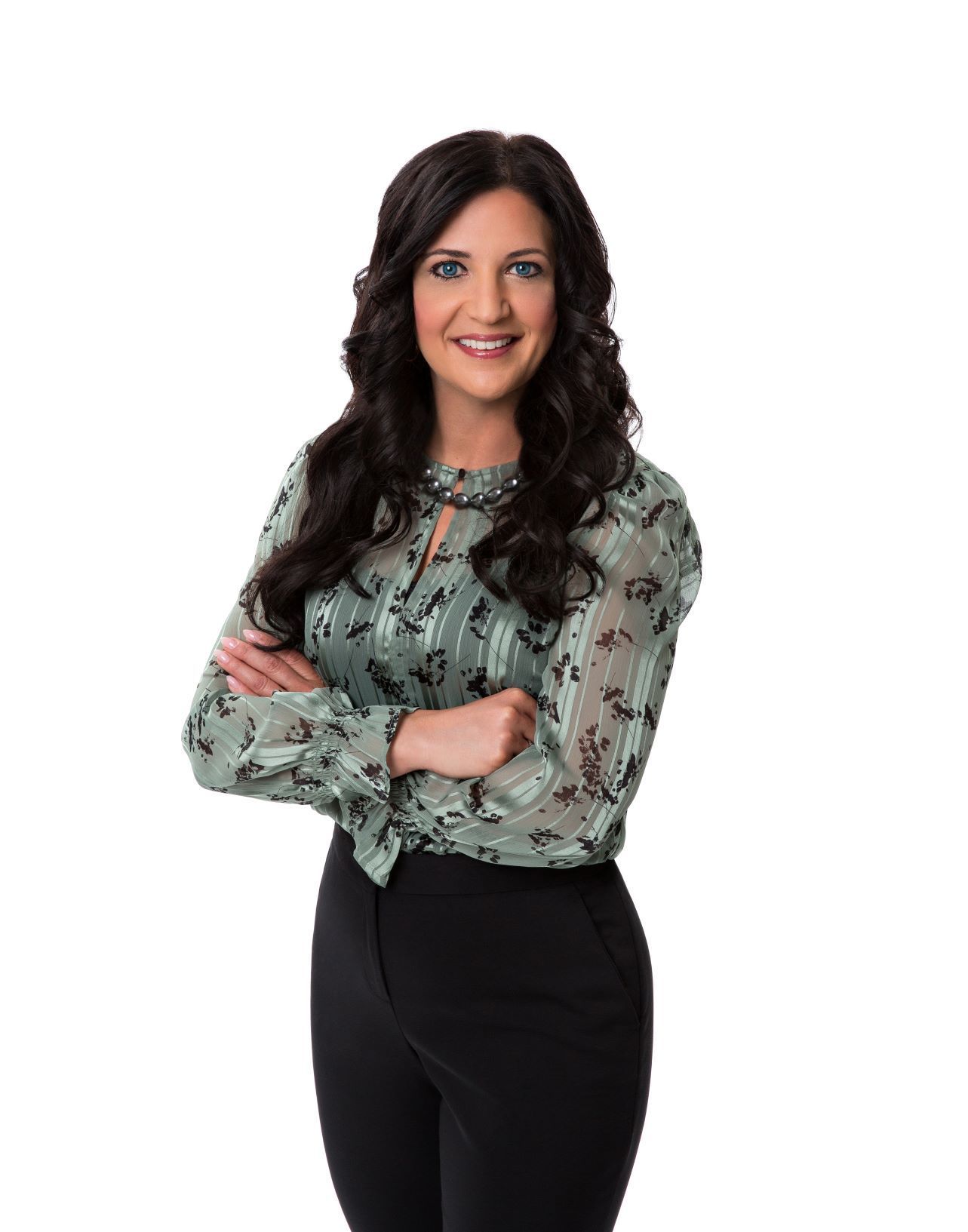 A woman in a green shirt and black pants is standing with her arms crossed.