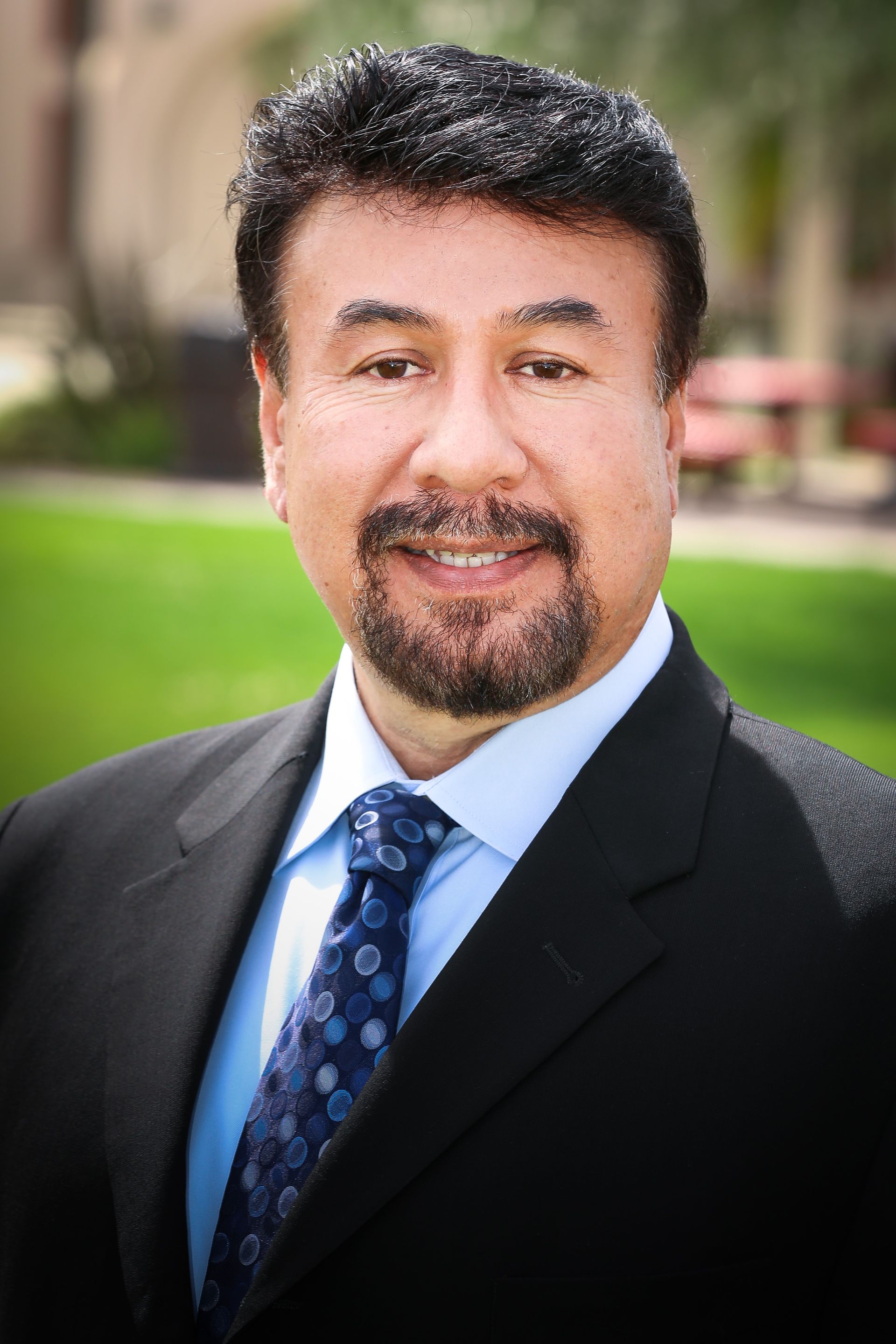 A man with a beard wearing a suit and tie is smiling for the camera.