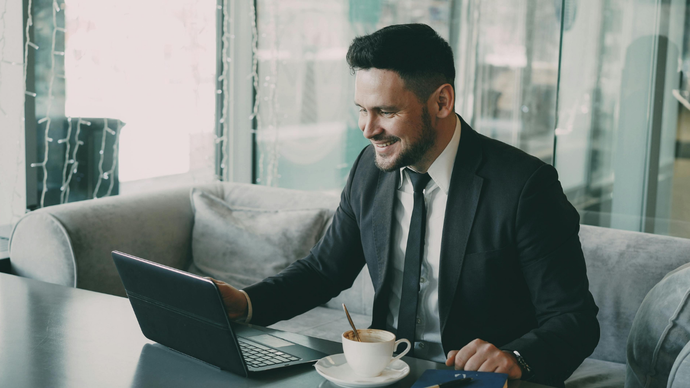 Person in white shirt and tie taking notes at a desk with laptop and charts.