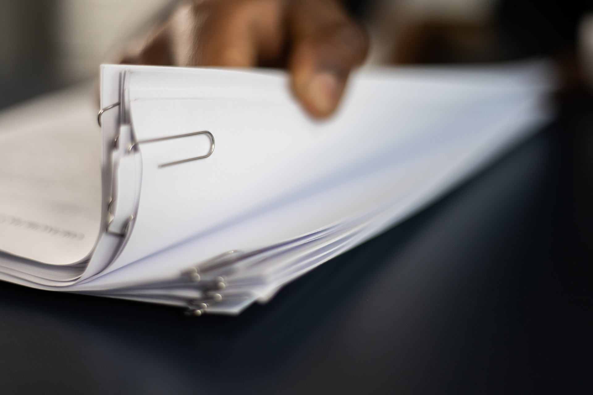 Hand flipping through a ring-bound stack of white papers with a blurred office background