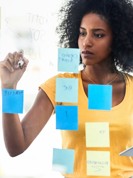 A woman is writing on a glass board with sticky notes